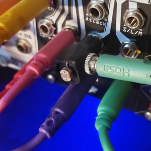 May include: Close-up of a synthesizer module with multiple colorful patch cables plugged in. The module has labels for "Hit", "Attack", "Bass", "A1+", "Teble", "S/L/M", and "ch".