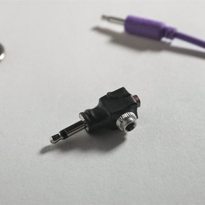 May include: A black 3.5mm to 3.5mm audio adapter with a red button. The adapter is designed to convert a single 3.5mm audio jack into two separate 3.5mm jacks.