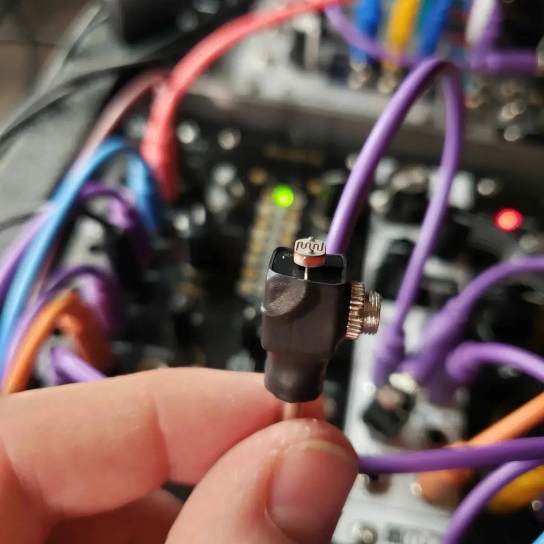 May include: Close-up of a black and silver electronic component with a small, rectangular, silver sensor on top. The component is connected to a purple cable.
