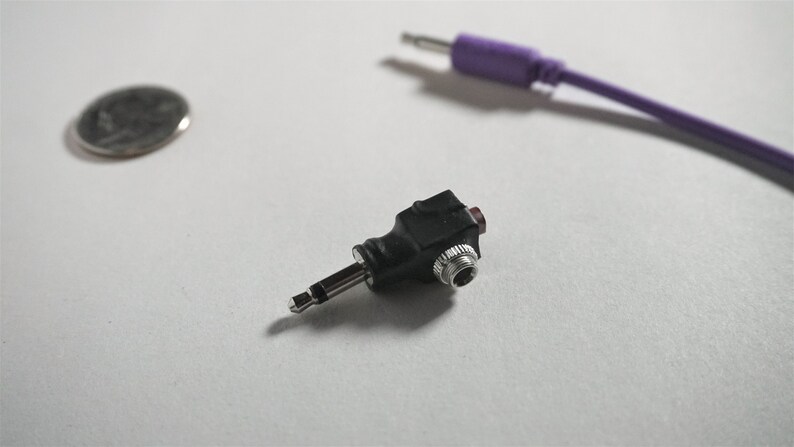 May include: A black 3.5mm to 3.5mm audio adapter with a red button. The adapter is designed to convert a single 3.5mm audio jack into two separate 3.5mm jacks.