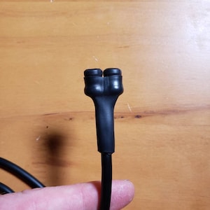 May include: Close-up of a black electrical cord with a split end, showing two black rubber caps.