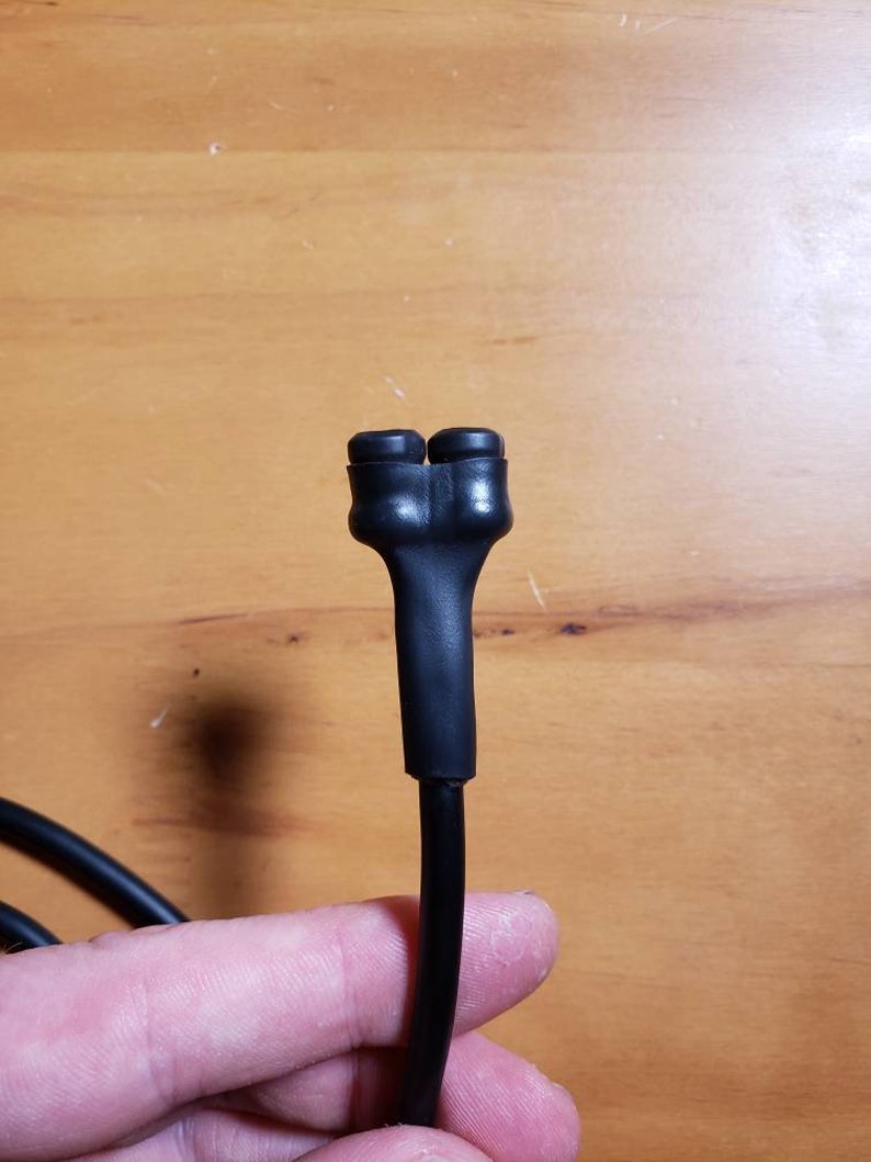 May include: Close-up of a black electrical cord with a split end, showing two black rubber caps.