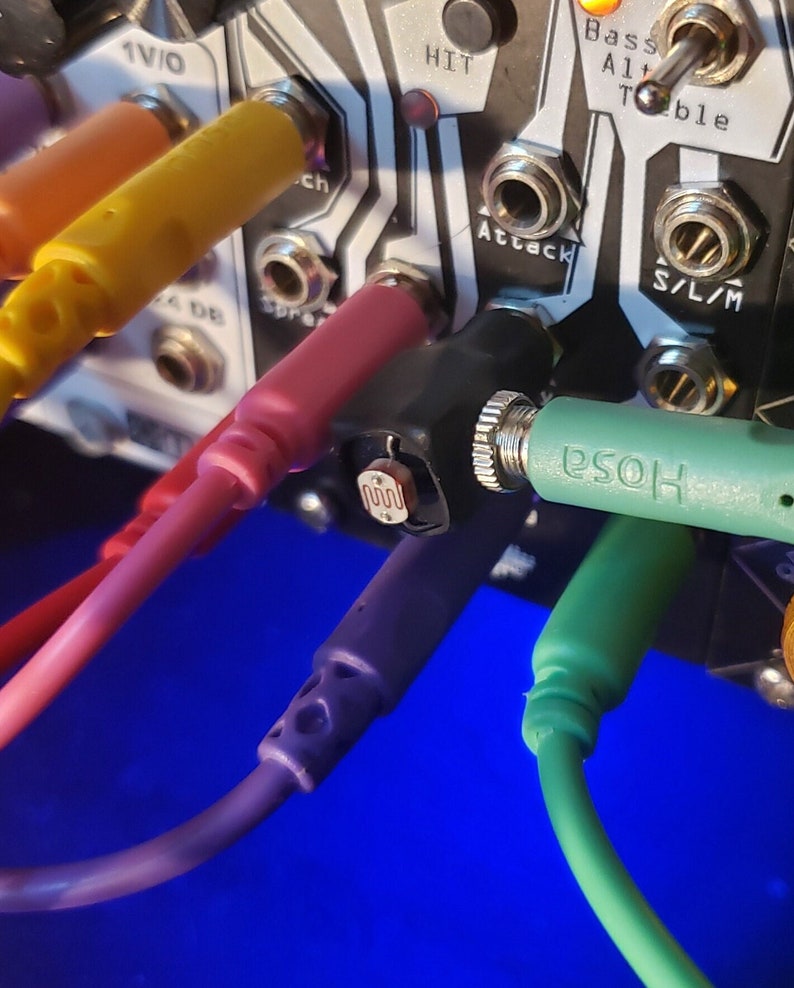 May include: Close-up of a synthesizer module with multiple colorful patch cables plugged in. The module has labels for "Hit", "Attack", "Bass", "A1+", "Teble", "S/L/M", and "ch".