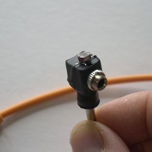 May include: A close-up of a black audio adapter with a silver 3.5mm jack. The adapter is connected to an orange cable.