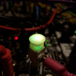 Pode incluir: Close-up de uma luz LED verde em um bot&atilde;o branco com um cabo rosa conectado. O bot&atilde;o est&aacute; etiquetado como "Fold" e faz parte de um sintetizador musical.