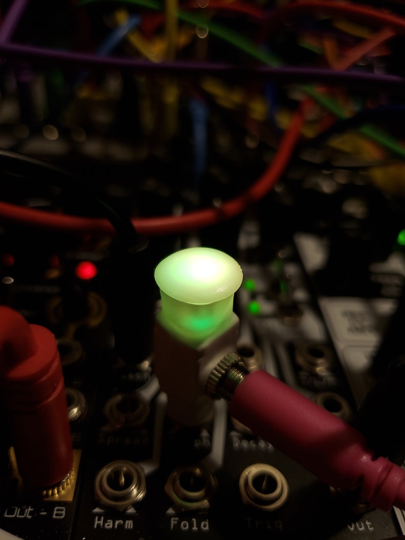Pode incluir: Close-up de uma luz LED verde em um bot&atilde;o branco com um cabo rosa conectado. O bot&atilde;o est&aacute; etiquetado como "Fold" e faz parte de um sintetizador musical.