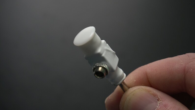 Pode incluir: Um conector de pl&aacute;stico branco com uma extremidade rosqueada prateada. O conector tem uma tampa redonda branca na parte superior.