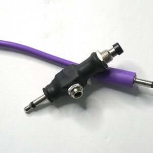 以下が含まれることがあります： 黒色のオーディオケーブルに紫色のケーブルが接続されています。黒色のケーブルは、一方の端にスイッチと6.35mmジャック、もう一方の端に6.35mmジャックが付いています。紫色のケーブルは、一方の端に6.35mmジャックが付いています。