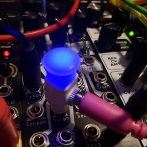 Pode incluir: Close-up de um m&oacute;dulo de sintetizador com uma luz LED azul, bot&otilde;es e conectores. O m&oacute;dulo tem etiquetas para "Pitch", "Spread", "Morph", "Dec", "Harm", "Fold" e "Trig".