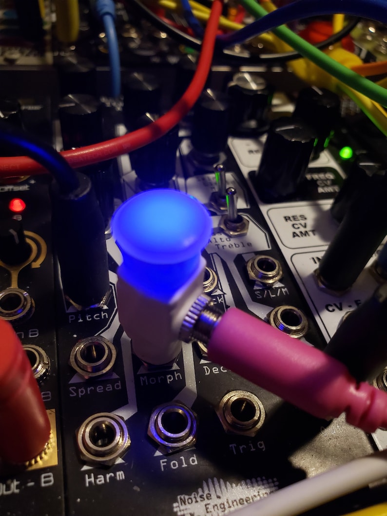 Pode incluir: Close-up de um m&oacute;dulo de sintetizador com uma luz LED azul, bot&otilde;es e conectores. O m&oacute;dulo tem etiquetas para "Pitch", "Spread", "Morph", "Dec", "Harm", "Fold" e "Trig".