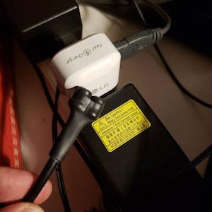 May include: A white LG fast charger with a black power cord and a yellow warning label that reads "Be careful! May become hot. Attention! Peut devenir chaud. 温度が高くなる場合があり ますので注意ください。 AC适配器可能发热! 请注意。"
