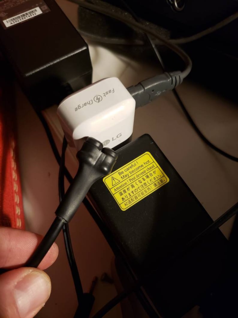May include: A white LG fast charger with a black power cord and a yellow warning label that reads "Be careful! May become hot. Attention! Peut devenir chaud. 温度が高くなる場合があり ますので注意ください。 AC适配器可能发热! 请注意。"