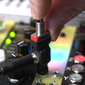 Op de afbeelding: Een close-up van een zwarte en zilveren audioconnector die in een rode en zwarte audio-aansluiting wordt gestoken. De connector wordt vastgehouden door een hand.