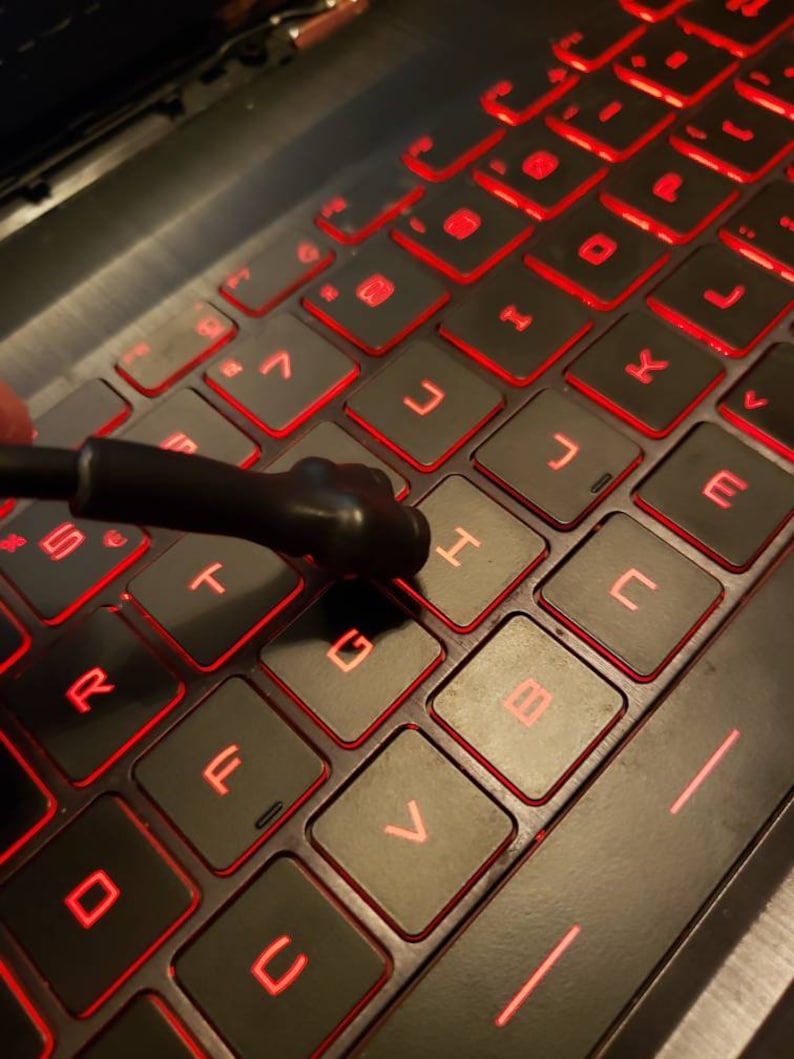 May include: A black laptop keyboard with red backlit keys. The keys are labeled with letters and numbers. A black tool is resting on the 'G' key.