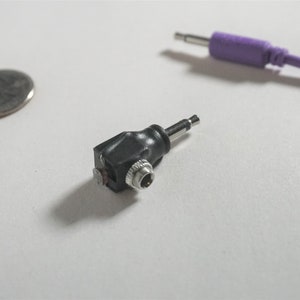 May include: A black 3.5mm to 1/4 inch audio adapter with a right-angle connector. The adapter is made of plastic and has a silver metal tip.