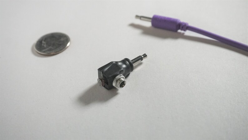 May include: A black 3.5mm to 1/4 inch audio adapter with a right-angle connector. The adapter is made of plastic and has a silver metal tip.