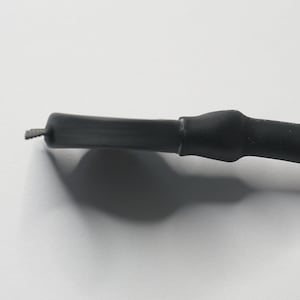 May include: Close-up of a black electrical wire with a black heat shrink tube covering the end.