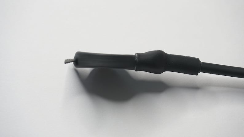 May include: Close-up of a black electrical wire with a black heat shrink tube covering the end.