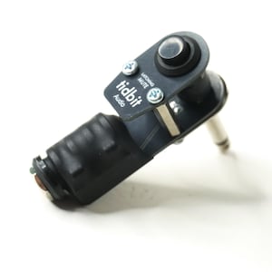 May include: A black audio cable adapter with a silver plug and a black button. The adapter has the text "tidbit Audio" and "Latching Mute" printed on it. The adapter is angled and appears to be new.