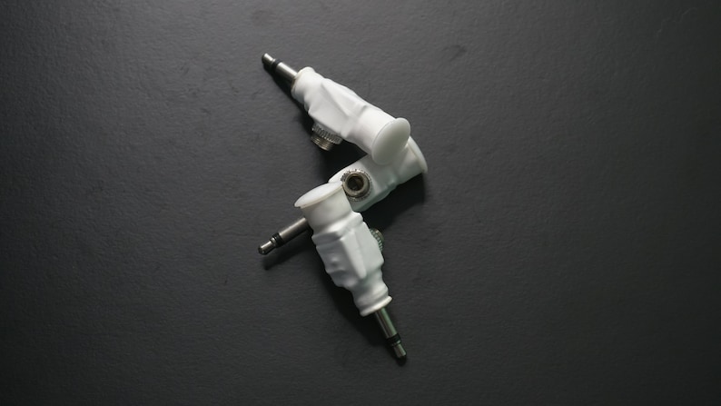 Pode incluir: Tr&ecirc;s adaptadores de &aacute;udio brancos com pontas de metal prateadas. Os conectores est&atilde;o dispostos em forma triangular.
