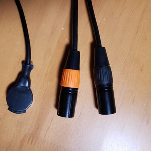 May include: Three black cables with different connectors. One connector is round and black, another is black with an orange ring, and the third is black with a gray ring.