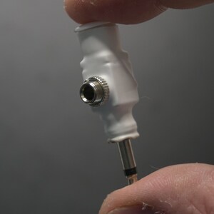 Pode incluir: Adaptador de pl&aacute;stico branco com uma tomada f&ecirc;mea de 3,5 mm em uma extremidade e uma tomada macho de 3,5 mm na outra extremidade.