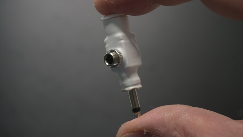 Pode incluir: Adaptador de pl&aacute;stico branco com uma tomada f&ecirc;mea de 3,5 mm em uma extremidade e uma tomada macho de 3,5 mm na outra extremidade.