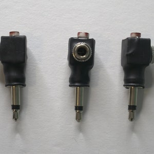 May include: Three black and silver right-angle audio adapters with a red plastic ring on the top. The adapters have a female jack on one end and a male plug on the other.