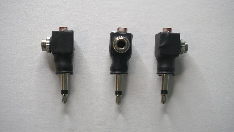 May include: Three black and silver right-angle audio adapters with a red plastic ring on the top. The adapters have a female jack on one end and a male plug on the other.