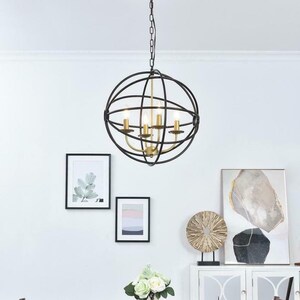 May include: A black metal globe chandelier with gold accents hangs over a dining table with two chairs. The table is made of dark wood and has a vase of white flowers in the center. There are two framed pictures on the wall behind the table.