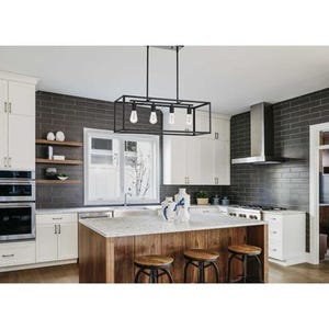 May include: A modern kitchen with white cabinets, a dark gray brick backsplash, and a wooden island with a granite countertop. A black rectangular light fixture hangs above the island. Three wooden stools are positioned at the island.