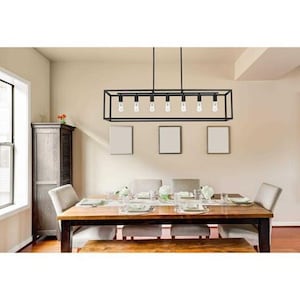 May include: A dining room with a rectangular wooden table set for a meal. Above the table hangs a black, rectangular light fixture with six exposed light bulbs. Beige chairs surround the table, and the walls are a neutral color.