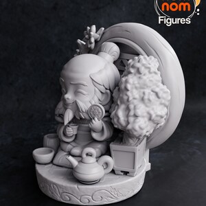 以下が含まれることがあります： 灰色の3Dプリントされた、ティーポットと小さな木のあるプラットフォームに座っている漫画のキャラクターのフィギュア。キャラクターはカップとクッキーを持っています。フィギュアには「CHIBI TURNTABLE」と「nom nom Figures」のラベルが貼られています。