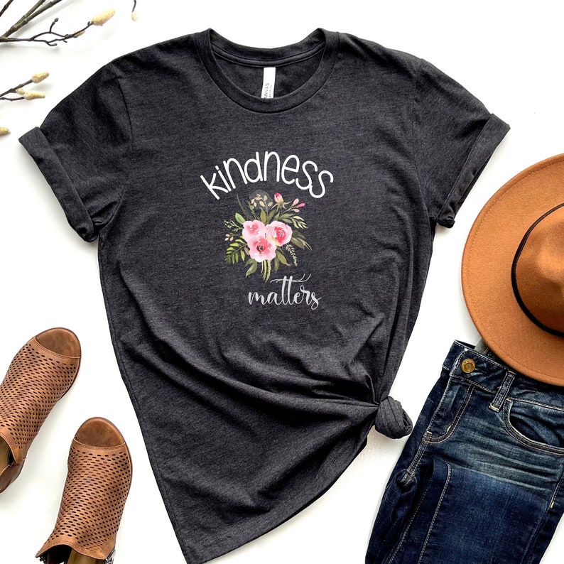 May include: A dark gray t-shirt with the text "kindness matters" in white lettering. A floral design with pink flowers is above the text.