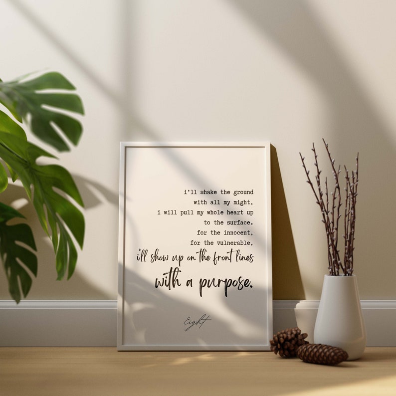 May include: A white framed print with a black and white typography quote that reads "I'll shake the ground with all my might, I will pull my whole heart up to the surface. For the innocent, for the vulnerable, I'll show up on the front lines with a purpose." The quote is signed "Eight".