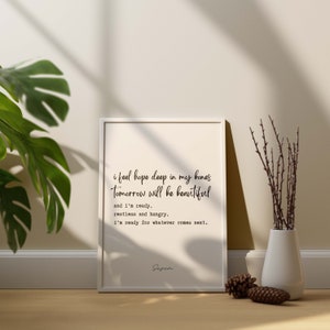 May include: A white framed print with a black and white inspirational quote that reads "i feel hope deep in my bones Tomorrow will be beautiful and i'm ready, restless and hungry. i'm ready for whatever comes next. Seven"