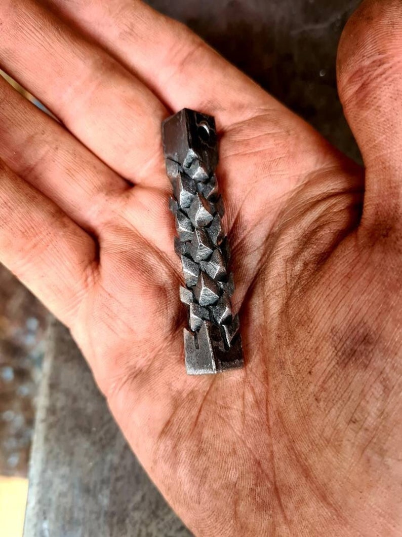 May include: A silver metal pendant with a geometric design. The pendant is made of small, triangular shapes that are connected together to form a chain-like pattern.