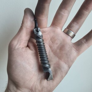 Pu&ograve; includere: Un apribottiglie in metallo ritorto con un portachiavi nero. L'apribottiglie &egrave; in metallo scuro e ha una superficie testurizzata.