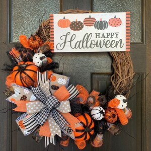 May include: A Halloween wreath with a brown grapevine base, decorated with orange, black, and white pumpkins, black and white polka dot ribbon, and a sign that reads "Happy Halloween".