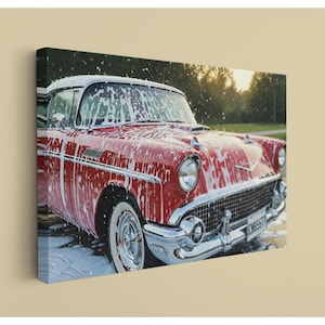 May include: A canvas print of a classic red vintage car covered in white suds. The car has chrome accents, white-walled tires, and a white roof. The image captures the car during a car wash, with a blurred background of trees and sunlight.