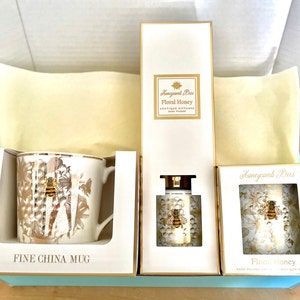 May include: A gift box set containing a white fine china mug with a gold bee design, a white diffuser bottle with a gold bee design, and two white boxes with gold bee designs. The boxes are labelled "Honeycomb Bees Floral Honey" and the mug is labelled "Fine China Mug".
