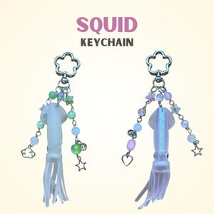 May include: Two squid keychains with flower-shaped clasps. The squid are white and iridescent, adorned with beads, stars, and a cloud charm. The text "SQUID KEYCHAIN" is above the keychains.