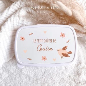 May include: A white rectangular lunch box featuring a printed design of a small bird, pink flowers, and brown leaves. The text reads "MOD&Egrave;LE : OISEAU" at the top and "LE PETIT GO&Ucirc;TER DE Giulia" in the center, written in a brown script font.