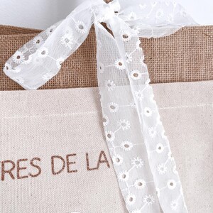 May include: A brown and beige tote bag with a white lace bow. The bag has the text "TRES DE LA" printed on the front.