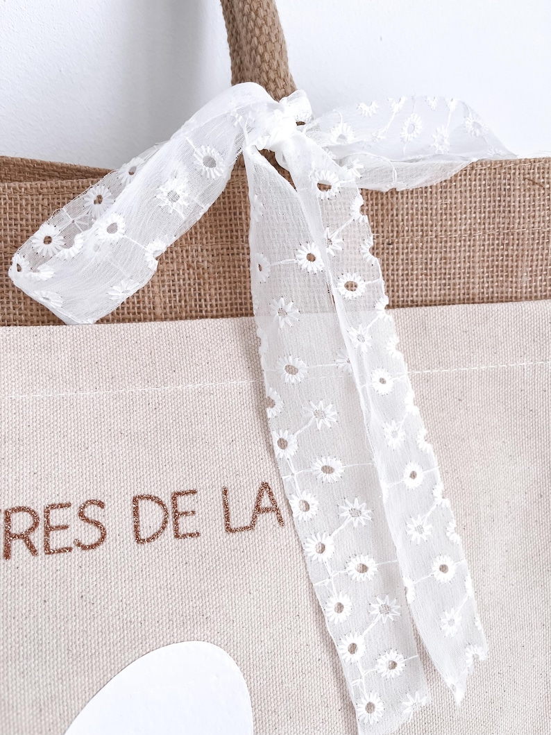 May include: A brown and beige tote bag with a white lace bow. The bag has the text "TRES DE LA" printed on the front.