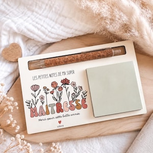 Peut inclure: Un organiseur de bureau en bois avec un stylo, un bloc-notes et un motif floral. Le texte dit "LES PETITES NOTES DE MA SUPER MAITRESSE Merci pour cette belle année LOUIS". Le stylo a un corps en liège. Le bloc-notes est vert clair.