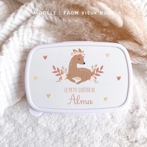 May include: A white rectangular lunch box featuring a brown fawn illustration with a floral crown, surrounded by small hearts and leaves. The text reads "MOD&Egrave;LE : FAON VIEUX ROSE" at the top and "LE PETIT GO&Ucirc;TER DE Alma" in the center of the lid.