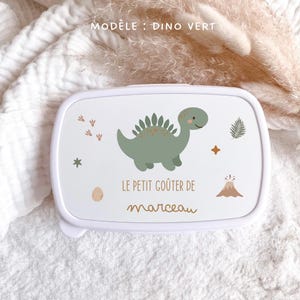 May include: A white rectangular snack box featuring a green dinosaur illustration, a small volcano, a fern leaf, and footprints. The text reads "LE PETIT GO&Ucirc;TER DE marceau" in brown lettering. The lid is white with rounded corners and a smooth finish.