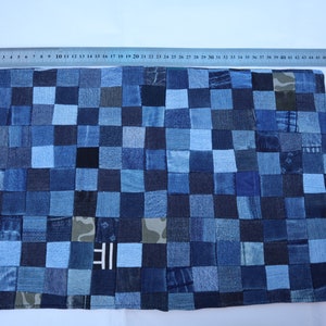 Könnte beinhalten: Ein blauer und weißer Patchwork-Platzdeckchen aus Jeansstoff. Das Platzdeckchen besteht aus vielen kleinen Quadraten aus Jeans, jedes in einem anderen Blauton. Das Platzdeckchen hat einen weißen Rand und die Buchstaben "IIE" sind in der Mitte sichtbar.