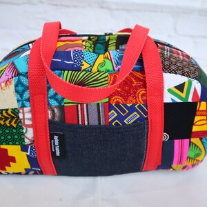 Pode incluir: Uma bolsa de viagem de lona colorida com alças vermelhas e um bolso de ganga. A bolsa é feita de vários tecidos de impressão africana e tem uma etiqueta que diz "Africa Fashion".